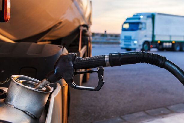 A truck is at a fueling station receiving fuel paid for by a fleet card while a truck waits its turn in the background.