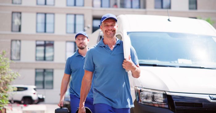 Two plumbers are geared up and heading into a job next to their company fleet van.