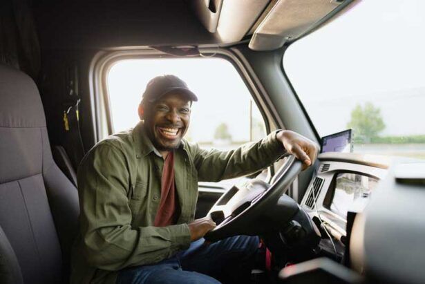 A happy truck driver in the cab of his fleet.